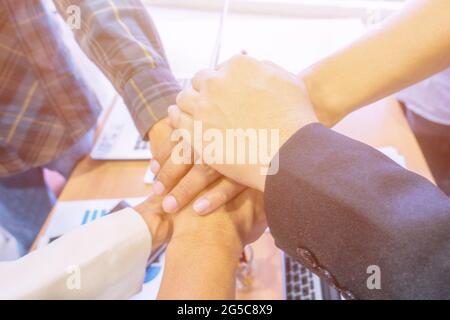 Geschäftsleute stapeln die Hände aus nächster Nähe, Büro-Desktop im Hintergrund, Konzept der Teamarbeit. Stockfoto