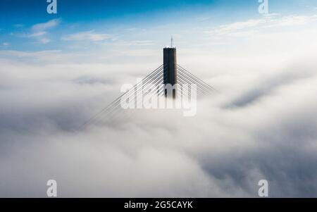 Die Spitze eines Turms der Queensferry Crossing Brücke schafft es, über starkem Nebel über dem Firth of Clyde, South Queensferry, Schottland, Großbritannien, aufzusteigen Stockfoto