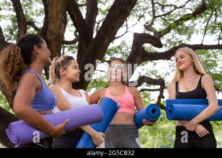 Glückliche junge multiethnische Frauen Freundinnen Gruppe entspannen und reden nach Yoga-Übung im Park am Wochenende Morgen. Leben nach covid. Stockfoto