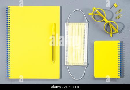 Verschiedene gelbe Büro- und Schulbedarf Bürobedarf mit Brille und medizinischer Maske auf grauem Hintergrund. Stockfoto