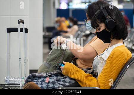 Bangkok, Thailand - Juni 29, 2021 : junge asiatische Frau Teenager trägt Schutzmaske für Coronavirus oder covid Virus und Musik hören. Stockfoto