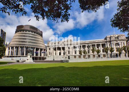 Das Bienenstock- und Parlamentsgebäude in Wellington, Nordinsel, Neuseeland, eingerahmt von Baumblättern und blauem Himmel darüber Stockfoto