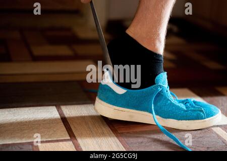 Nahaufnahme Mann versuchen, auf die blauen Sneaker Schuhe mit der Hilfe zu setzen Stockfoto