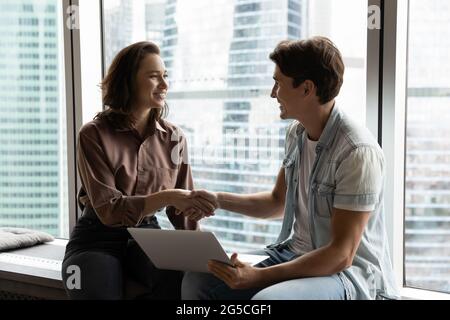 Lächelnde junge Teamleiterin schüttelt sich die Hände mit dem männlichen Mitarbeiter. Stockfoto