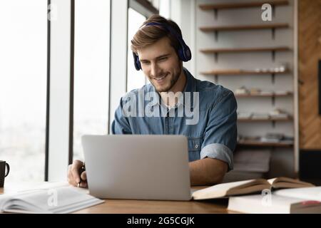 Lächelnder junger Mann mit Kopfhörern, der einen lehrreichen Vortrag ansieht. Stockfoto