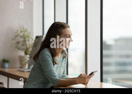 Glückliche junge Frau, die Smartphone hält und am Tisch in der Küche sitzt. Stockfoto