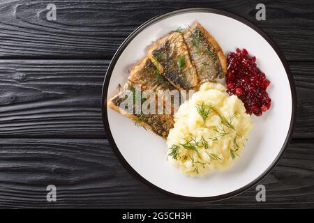 Gebratene Heringfilets mit Kartoffelpüree und Preiselbeersoße aus der Nähe auf einem Teller auf dem Tisch. Horizontale Draufsicht von oben Stockfoto