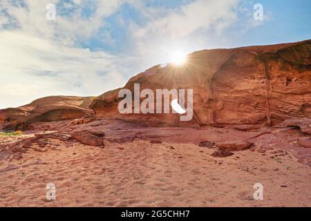 Kleiner Bogen oder kleine Felsenfensterbildung in der Wadi Rum Wüste, strahlende Sonne scheint darüber Stockfoto