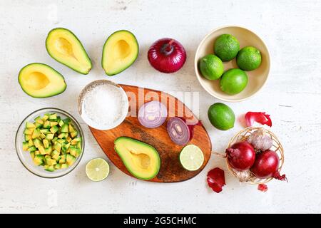 Avocado-Hälften, Stücke, Limetten und Zwiebeln, Tasse mit Salz - Grundzutaten der Guacamole auf weißem Brett, flaches Lay-Foto Stockfoto