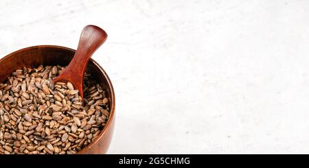 Segened Milch Distel Samen - Silybum Marianum - in kleinen Holzschale mit Löffel, auf weißem Stein wie Brett, Platz für Text rechts Stockfoto