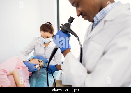 Professionelle Krankenschwester und afro-amerikanischer Gastroenterologe, der im Krankenhaus eine Endoskopie für junge weibliche Patienten durchführt. Gesundheitswesen und Medizin. Stockfoto