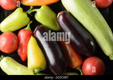 Paprika, Tomaten, Zucchini, Gemüse auf einem schwarzen Backblech verteilt. Draufsicht. Stockfoto