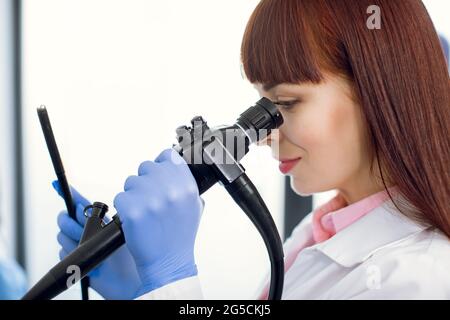 Instrument für die Endoskopie in den Händen einer ziemlich jungen kaukasischen Ärztin, die gastrointestinale faseroptische Endoskopie durchführt. Nahaufnahme im Hochformat. Stockfoto