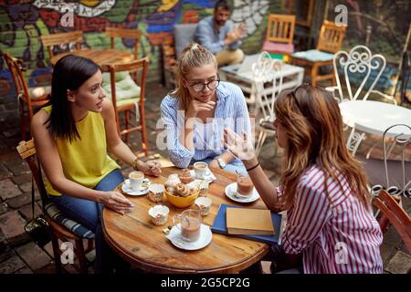 Gruppe von jungen erwachsenen kaukasischen Freundinnen reden und lachen im Café im Freien, trinken Kaffee. Soziales Konzept Stockfoto