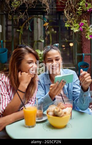 Eine Freundin zeigt einem anderen etwas auf ihrem Handy, das im Café im Freien sitzt Stockfoto