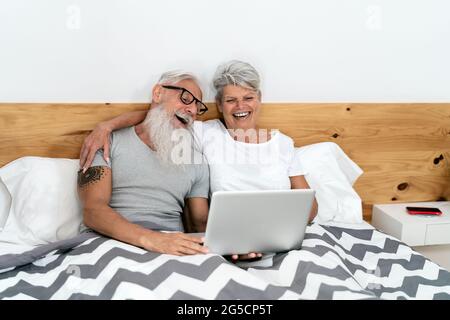 Glückliches Seniorenpaar, das Spaß daran hat, einen Laptop im Bett zu sehen - Technik und Lifestyle-Konzept für ältere Menschen Stockfoto