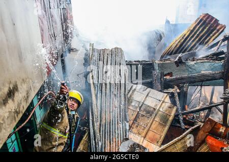 Quezon City. Juni 2021. Ein Feuerwehrmann versucht am 26. Juni 2021, einen Brand in einem Wohngebiet in Quezon City auf den Philippinen zu löschen. Quelle: Rouelle Umali/Xinhua/Alamy Live News Stockfoto