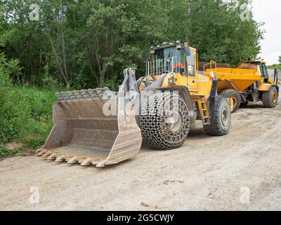 Bulldozer-Eimer für schwere Lader. Traktorlader mit schützenden Radketten auf Reifen wartet am Sandkasten Stockfoto