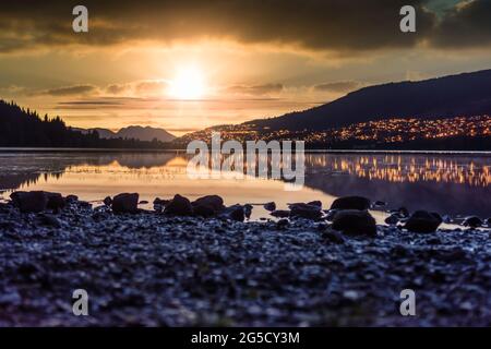 Sonnenuntergang am Rotevatnet in Volda, Norwegen, mit Zitronenlichtern im Hintergrund und Steinen im Vordergrund Stockfoto
