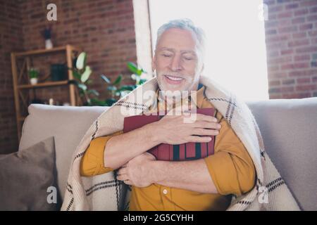 Foto einer zufriedenen Person sitzen auf der Couch geschlossene Augen strahlend Lächeln Hände halten umarmende Buch Freizeit drinnen Stockfoto