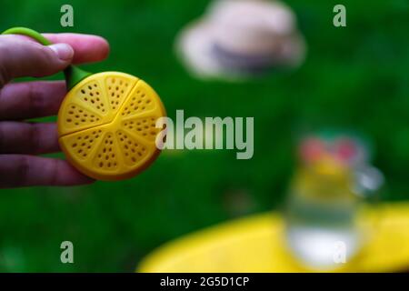 Defocus Hand hält Dummy Zitrone über Glas Krug Limonade mit Scheibe Zitrone und Blätter der Minze auf natürlichem grünem Hintergrund. Krug des Sommers Stockfoto