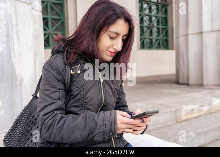 Porträt einer jungen lateinerin, die auf der Straße ihr Handy überprüft. Technologiekonzept Stockfoto