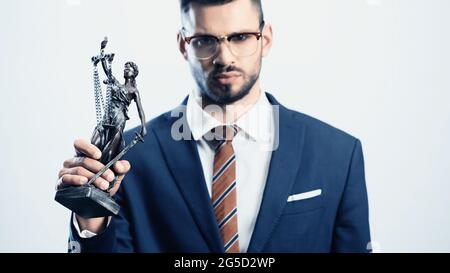 Verschwommener Geschäftsmann, der eine Justizstatuette hält, während er die Kamera isoliert auf Weiß betrachtet Stockfoto