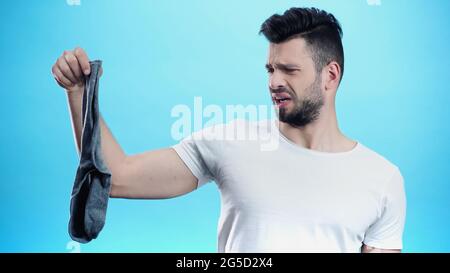 Angewiderter Mann mit stinkenden Socken isoliert auf blau Stockfoto
