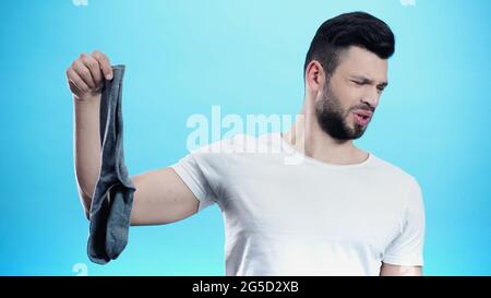 Mann fühlt sich angewidert, während er stinkende Socken isoliert auf Blau hält Stockfoto