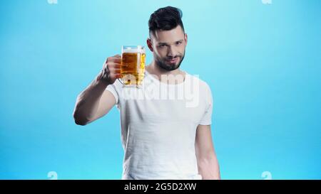 Zufriedener Mann, der einen Becher kaltes Bier auf Blau hält Stockfoto