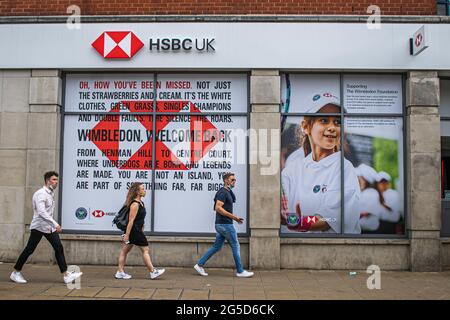 London, Großbritannien. Juni 2021. Fußgänger kommen an einer HSBC-Bankfiliale im Stadtzentrum von Wimbledon vorbei, die die willkommene Rückkehr der Wimbledon Championships 2021 anwirbt, die am Montag, dem 28. Juni, beginnen soll. Die Tennismeisterschaften sind zurück, nachdem sie im vergangenen Jahr zum ersten Mal seit dem zweiten Weltkrieg aufgrund der Covid-19-Pandemie abgesagt wurden. Die Organisatoren der Weltmeisterschaft haben gesagt, dass die Kapazität um 50 % reduziert wird und die Zuschauer Tickets vorbestellen müssen. Kredit: amer ghazzal/Alamy Live Nachrichten Stockfoto