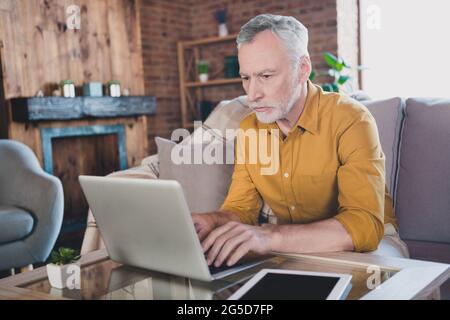 Foto einer konzentrierten, gealterten Person, die auf der Couch sitzt, verwenden Sie einen Laptop, um von zu Hause aus zu schreiben Stockfoto