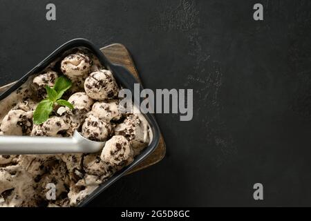 Hausgemachtes, zuckerfreies, cremiges Eis mit Keksen im Behälter auf schwarzem Hintergrund mit Platz zum Kopieren. Blick von oben. Leckere Kinder Dessert ohne Stockfoto