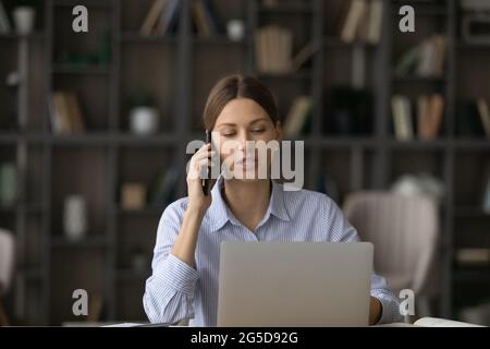 Fokussierte junge Geschäftsfrau, die Telefonanruf hält und am Computer arbeitet. Stockfoto