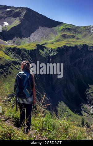Rückansicht einer Wandererin mit einem großen Rucksack, die an einem sonnigen Tag am Rande eines felsigen Hügels steht Stockfoto