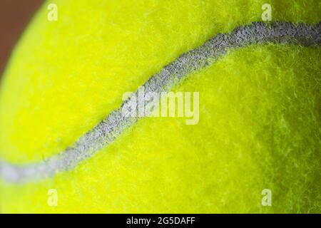 Makro-Nahaufnahme eines fluoreszierenden gelben (optisch gelben) Tennisballs, der die faserige Filzabdeckung und das weiße geschwungenes Oval zeigt Stockfoto