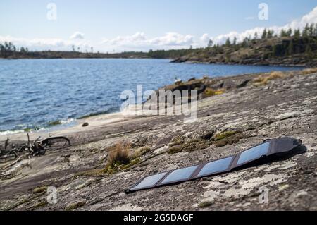 Tragbare Sonnenkollektoren liegen am Steinufer des Sees und sammeln Energie. Moderne Technologien und Hosenträger des Lebens. Stockfoto