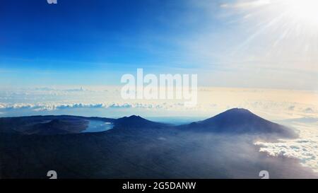 Blick vom Flugzeugfenster. Luftaufnahme von Agung - höchster Gipfel der Insel Bali, Mount Abang, aktiver Vulkan Batur mit vulkanischem See in Caldera. Stockfoto