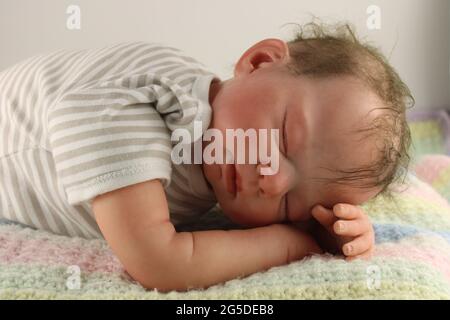Schlafender Junge auf Strickdecke liegend, Elternschaft Konzept durch eine wiedergeborene Puppe dargestellt Stockfoto