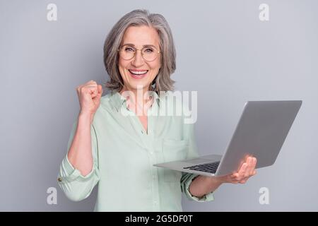 Porträt von attraktiven trendigen fröhlich grauhaarige Frau mit Laptop feiern Spaß isoliert über grauen Pastellfarben Hintergrund Stockfoto