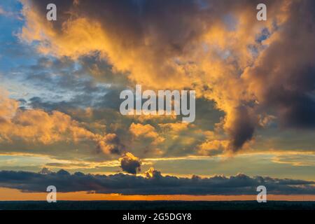 Spektakulärer gelb-oranger Sonnenuntergang über dem Wald. Die Sonne geht unter und erhellt die dicken Wolken mit Strahlen Stockfoto