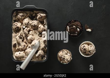 Frische cremiges Eis mit Cookies im Behälter auf schwarzem Hintergrund. Draufsicht. Speicherplatz kopieren. Dessert ohne Zucker für sauberes Essen. Stockfoto