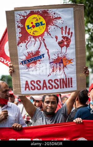 Novara, Italien. 26. Juni 2021. Ein Demonstrator hält ein Plakat mit der Aufschrift „Lidl, Texprint, FedEx, Attentäter!“ Während einer von der Gewerkschaft SI Cobas organisierten Demonstration gegen die Tötung von Adil Belakhdim. Der Gewerkschafter Adil Belakhdim starb am Freitag, dem 18. Juni, nachdem er von einem Lastwagen getroffen worden war, der die Blockade, die von den Arbeitern während eines Streiks vor dem Lidl-Lager in Biandrate bei Novara organisiert wurde, erzwungen hatte. Kredit: Nicolò Campo/Alamy Live Nachrichten Stockfoto