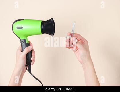 Körperpflege, Beauty-Konzept. Weibliche Hände mit Nagelschere und Haartrockner auf beigefarbenem Hintergrund. Draufsicht Stockfoto