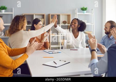 Glückliche Geschäftsfrauen, die einen Deal machen und sich gegenseitig am Tisch in einem Gruppentreffen hochhalten Stockfoto