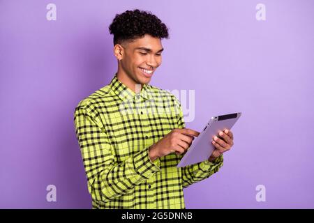 Foto von charmanten positiven afro amerikanischen Mann aussehen Tablette lesen gute Laune Lächeln auf lila Hintergrund isoliert Stockfoto