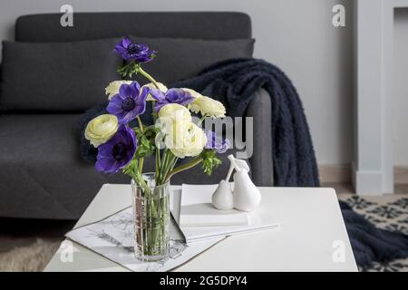 Bouquet von weißem Ranunculus und blauer Anemone in der Vase auf einem weißen Couchtisch neben dem Sofa. Die Bücher und die Zeitschrift. Schatten. Stockfoto
