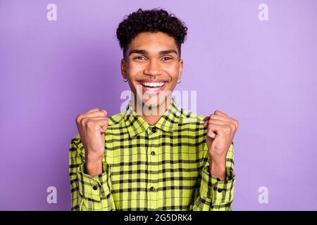 Foto von glücklichen charmanten dunklen Haut Brünette Mann heben Fäuste gute Laune gewinnen isoliert auf violetten Hintergrund Stockfoto