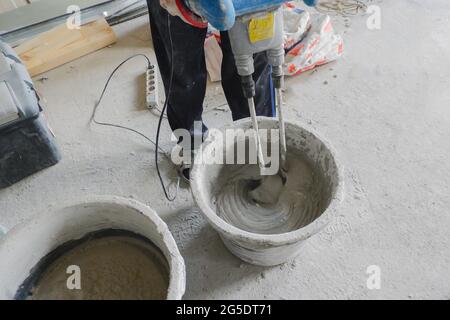 Der Bauherr mischt das Baugemisch in einem Behälter zur Führung der Lösung mit einem Mischer, Stockfoto