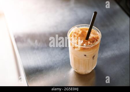 Blick aus der Perspektive auf einen eisgekühlten Kaffee-Latte mit Stroh auf einer Stahltheke im Kaffeehaus. Erfrischende und belebende koffeinhaltige Getränke auf heißer Summe Stockfoto